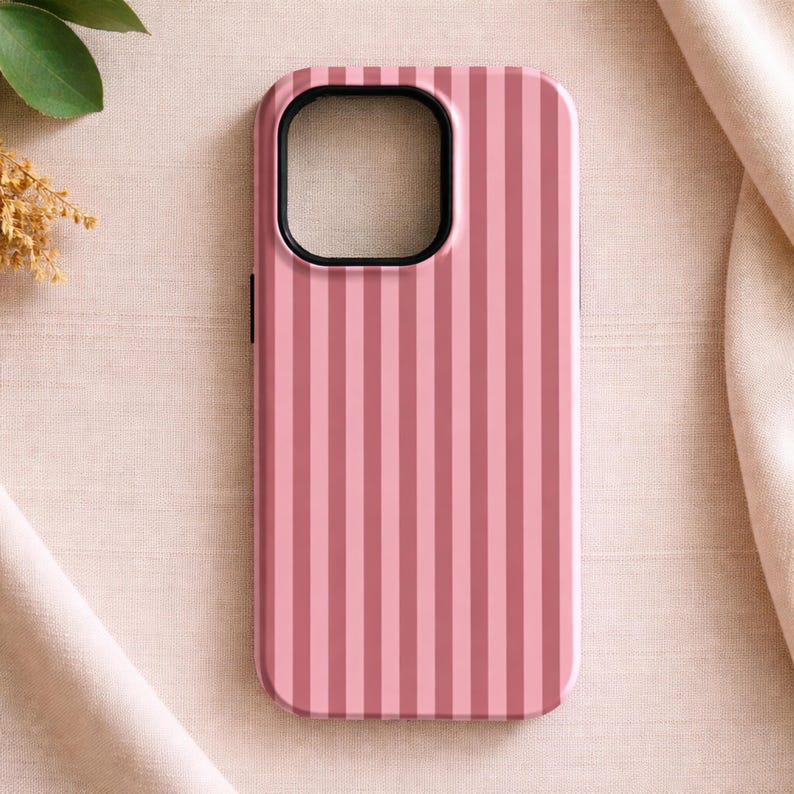 May include: Pink and light pink striped phone case. The case has a black border around the camera and screen openings. The case is made of a hard plastic material.