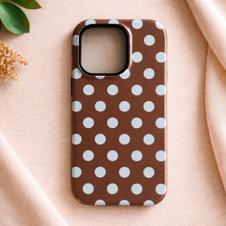 May include: A brown phone case with a pattern of light blue polka dots. The case has a black border around the camera cutout. The phone case is a protective accessory for a smartphone.