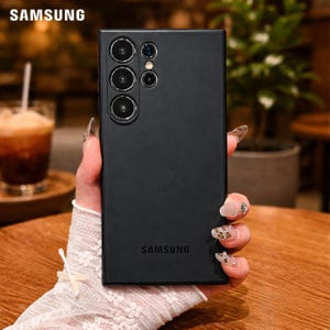 May include: A black Samsung phone case with multiple camera lenses. The Samsung logo is visible at the top and bottom of the case. The phone case is held by a person.