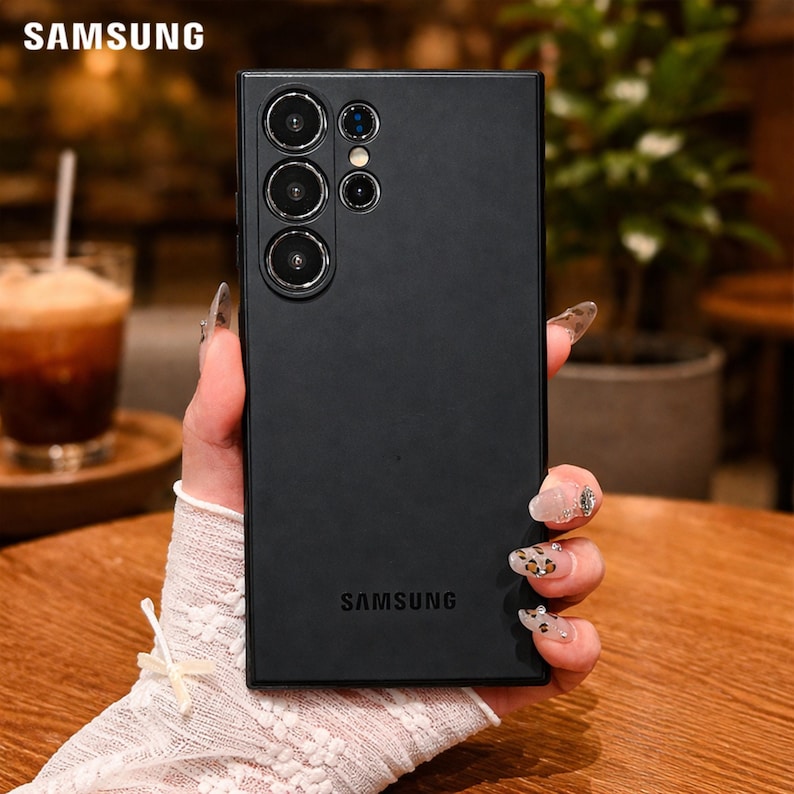 May include: A black Samsung phone case with multiple camera lenses. The Samsung logo is visible at the top and bottom of the case. The phone case is held by a person.