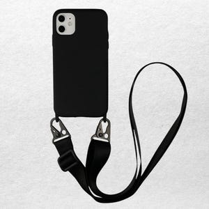 May include: Black phone case with a matching black strap. The case has a camera cutout and metal clips to attach the strap. The strap is adjustable and can be worn around the neck or across the body. The phone case is designed to fit a smartphone.