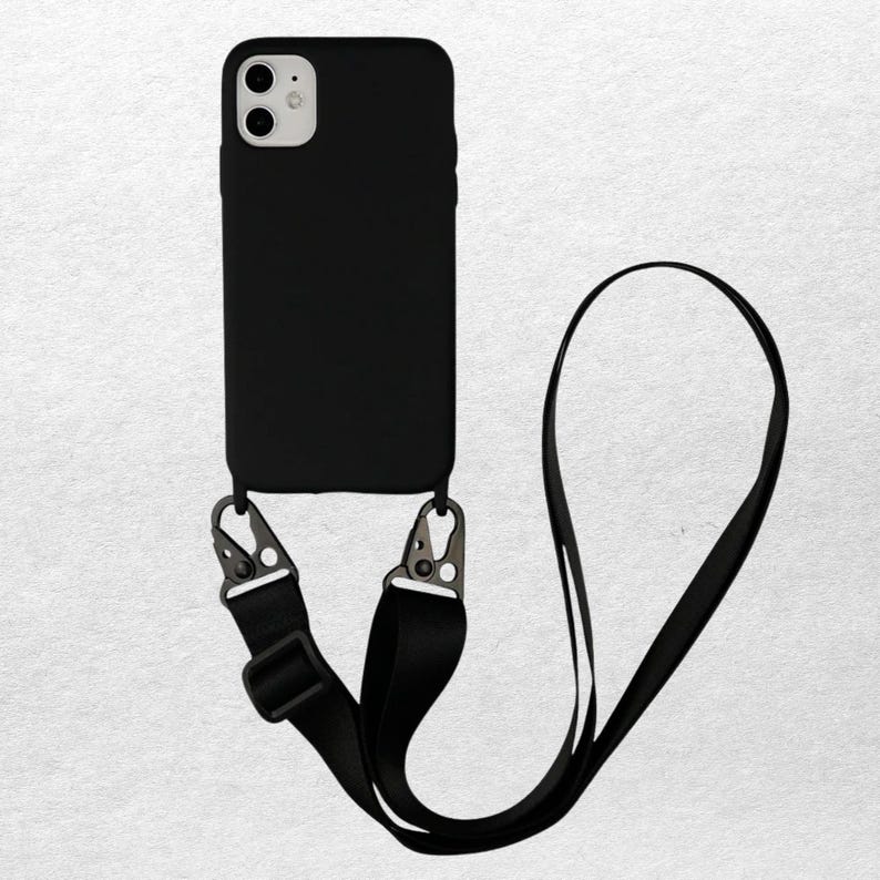May include: Black phone case with a matching black strap. The case has a camera cutout and metal clips to attach the strap. The strap is adjustable and can be worn around the neck or across the body. The phone case is designed to fit a smartphone.