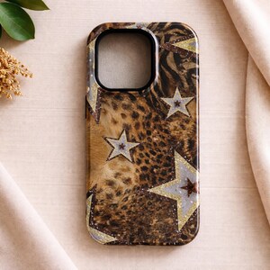May include: A phone case with a brown and tan leopard print design, accented with silver and gold glitter stars. The case has a black camera cutout and is made of a hard, protective material.
