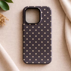 May include: A dark gray phone case with a pattern of small, evenly spaced, light beige polka dots. The case has a camera cutout and a smooth, glossy finish. The phone case is designed to protect the phone.