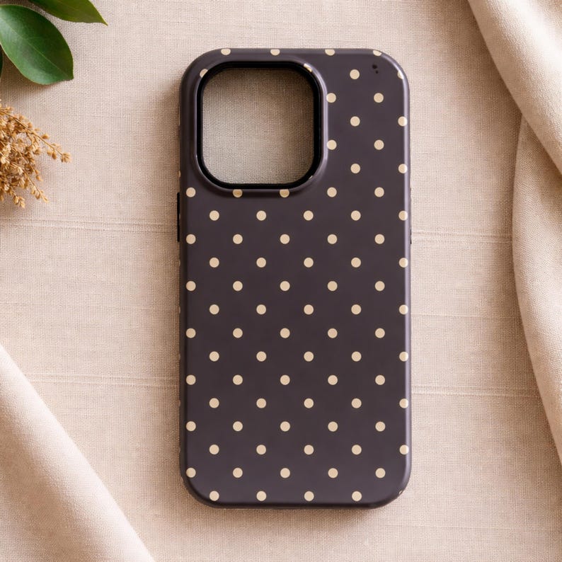 May include: A dark gray phone case with a pattern of small, evenly spaced, light beige polka dots. The case has a camera cutout and a smooth, glossy finish. The phone case is designed to protect the phone.