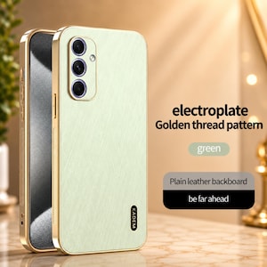 May include: A light green phone case with a gold-colored frame. The case has a textured back and features a camera module with three lenses. The text on the case reads "KADEM". Additional text includes "electroplate Golden thread pattern" and "Plain leather backboard".