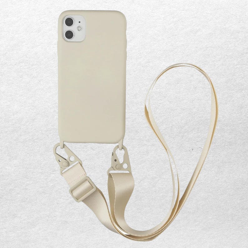 May include: A solid beige smartphone case with a dual-lens camera cutout at the top left. The case features two metal lobster claw clasps at the bottom, attached to a matching beige adjustable fabric strap that forms a long loop for carrying.