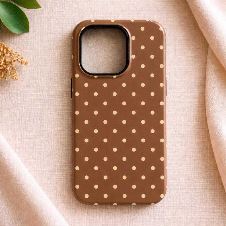 May include: A brown phone case with a repeating pattern of small, evenly spaced, cream-colored polka dots. The case has a camera cutout and a black border around the camera opening.