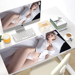 May include: A computer desk setup featuring a large mousepad with a printed image of a woman in a nurse's uniform. The desk also includes a computer monitor, keyboard, tissue box, and a cup of coffee.