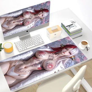 May include: A computer setup featuring a large monitor and a matching mousepad. Both display a detailed illustration of a woman with red and white hair, tattoos, and floral accents. A keyboard, tissue box, and coffee cup are also visible.