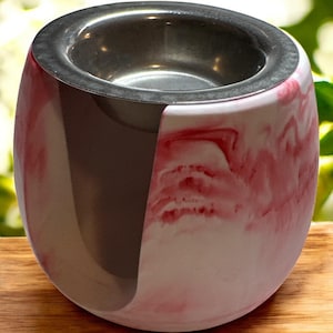 Könnte beinhalten: Ein dekorativer Kerzenhalter mit Edelstahl-Innenraum und marmoriertem Äußeren. Das Äußere weist ein Wirbelmuster aus Weiß und Rot auf, das eine einzigartige Ästhetik erzeugt. Der Halter hat eine abgerundete Form.