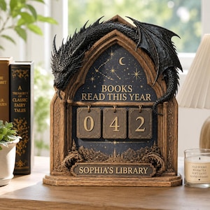 Puede incluir: Un contador de libros de madera con temática de dragón que muestra el texto "BOOKS READ THIS YEAR" y el número "042". El contador tiene un fondo azul oscuro con estrellas y una luna creciente. La base dice "SOPHIA'S LIBRARY".