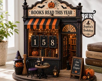 May include: A miniature Halloween-themed bookstore display featuring a sign that reads BOOKS READ THIS YEAR with the numbers 158, a hanging sign for Sophia's Bookshop, a striped awning, a small table with a mug, and a chalkboard sign saying One More Chapter.