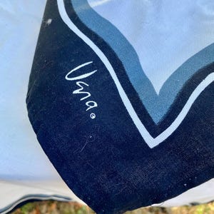 May include: A white fabric with a black and blue trim. The trim has a wavy pattern and the word "Uma" is written in black on the fabric.