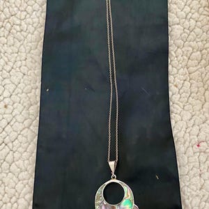 Pu&ograve; includere: Una collana con catena d'argento con un grande ciondolo in madreperla di abalone iridescente. Il ciondolo ha la forma di un cerchio con un cerchio pi&ugrave; piccolo tagliato al centro. Il ciondolo &egrave; circondato da cerchi pi&ugrave; piccoli in madreperla di abalone.