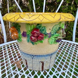 May include: A ceramic planter with a yellow rim and a design of fruit and leaves in shades of green, red, orange, and purple.