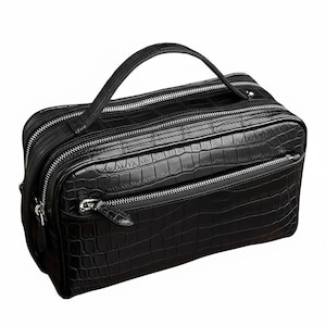 以下が含まれることがあります： 黒色の革製トラベルバッグ。クロコダイル柄のテクスチャが特徴です。複数のジッパー付きコンパートメントと、持ち運び用のトップハンドルが付いています。ジッパーはシルバー色で、バッグは長方形です。