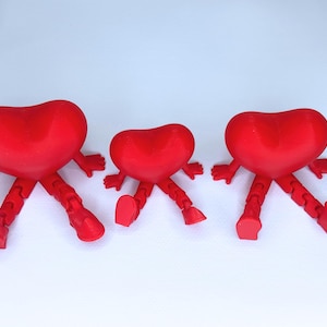 Puede incluir: Tres figuras rojas en forma de corazón con brazos y piernas articulados. Los corazones están posados como si estuvieran reclinados, con los brazos y las piernas extendidos. Las figuras están sobre un fondo blanco.