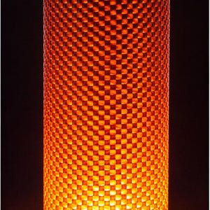 May include: A cylindrical lamp with a checkered pattern, emitting a warm orange glow. The lamp sits on a wooden base. The lamp's height is approximately 12 inches.