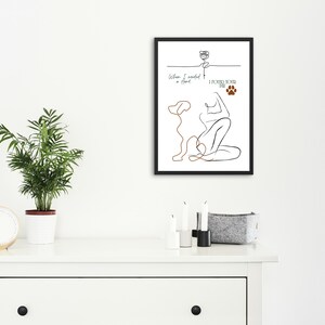 Könnte beinhalten: Ein gerahmter Kunstdruck mit einer minimalistischen Strichzeichnung einer Person und eines Hundes. Das Kunstwerk enthält den Text "When I needed a hand, I found your paw." Der Druck wird auf einer weißen Kommode mit einer Pflanze und einer Uhr angezeigt.
