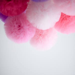 Puede incluir: Un grupo de pompones de tul rosa, morado y blanco colgando del techo.