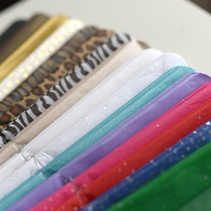K&ouml;nnte beinhalten: Ein Stapel bunten Seidenpapiers in verschiedenen Mustern und Farben, darunter Leopardenmuster, Zebramuster, Wei&szlig;, T&uuml;rkis, Lavendel, Rosa, Rot, Blau und Gr&uuml;n.