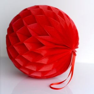 May include: A red paper honeycomb ball with a red ribbon attached. The ball is made of many small, overlapping circles of paper.