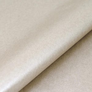 May include: A sheet of light beige paper with a smooth, matte texture. The paper is folded diagonally, creating a sharp crease that runs from the top right to the bottom left, revealing a subtle gradient of light and shadow across the surface.