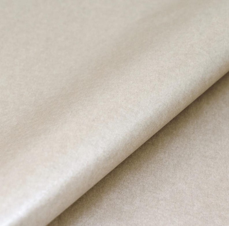 May include: A sheet of light beige paper with a smooth, matte texture. The paper is folded diagonally, creating a sharp crease that runs from the top right to the bottom left, revealing a subtle gradient of light and shadow across the surface.