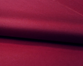 Può includere: Un tessuto color magenta intenso a tinta unita con una consistenza liscia e opaca. Il materiale è ripiegato su se stesso, creando una morbida piega orizzontale al centro che proietta un'ombra sottile, evidenziando il colore uniforme.