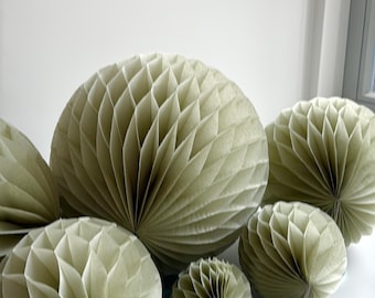 May include: A set of six green paper honeycomb balls of various sizes. The balls are arranged in a semi-circle on a white surface.