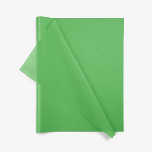 May include: A rectangular sheet of bright green tissue paper with a smooth, semi-translucent texture. The paper is folded diagonally across the center, creating a triangular flap that reveals a slightly lighter shade of green where it overlaps.