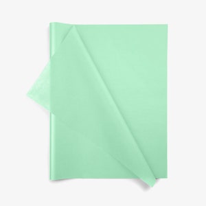 May include: A stack of rectangular mint green tissue paper sheets. The top sheet is partially folded over, revealing the thin, semi-translucent texture of the paper. The material has a smooth, matte finish and a consistent light green color throughout.