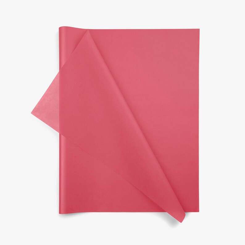 May include: A rectangular sheet of solid dark pink tissue paper with a smooth, matte texture. The paper is folded over at the top left corner, revealing a slightly more translucent layer underneath the main surface of the vibrant pink sheet.
