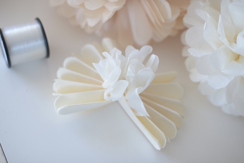 May include: A white paper flower with a layered, fan-like design. The flower is made from multiple layers of white paper that are folded and layered to create a three-dimensional effect. The flower is a popular craft project and can be used for a variety of purposes, such as decorating a home or adding a touch of elegance to a special event.