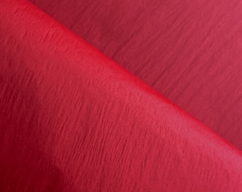 Può includere: Un materiale in tessuto o carta di colore rosso intenso con una trama che presenta un sottile motivo a pieghe verticali. La superficie mostra una tonalità cremisi costante con variazioni di luce e ombra create dalle pieghe del materiale.