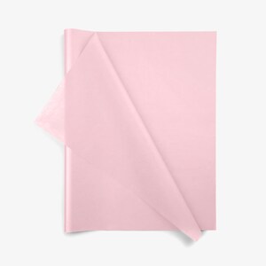 May include: A stack of rectangular light pink tissue paper sheets. The top sheet is partially folded over at the left corner, revealing the thin, semi-translucent texture of the paper. The material is smooth, matte, and uniform in color.