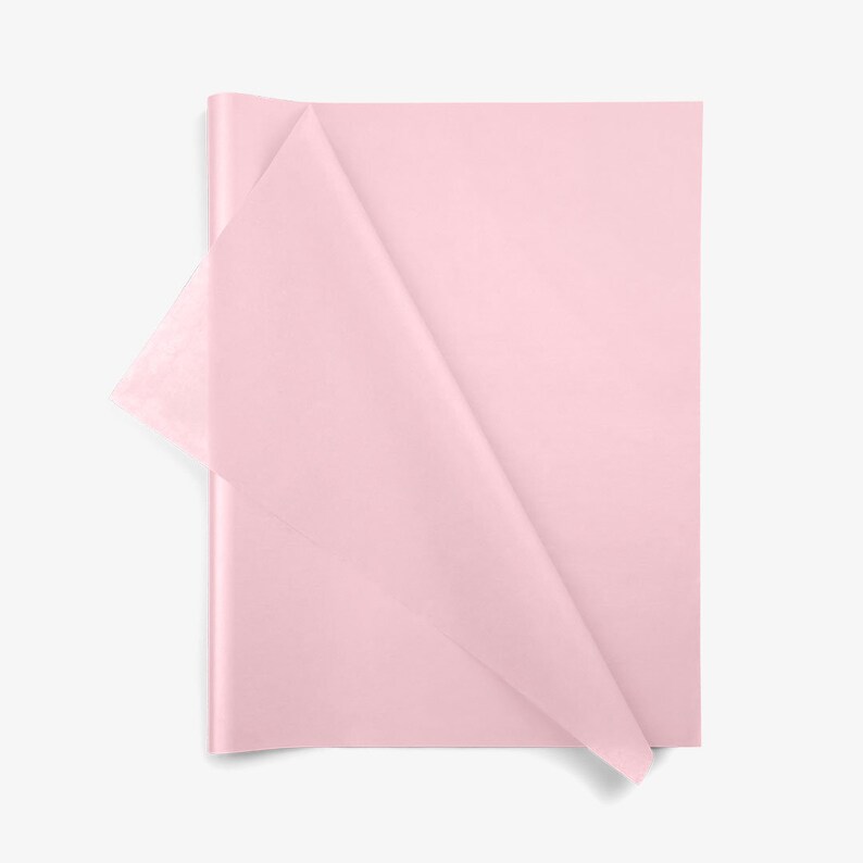 May include: A stack of rectangular light pink tissue paper sheets. The top sheet is partially folded over at the left corner, revealing the thin, semi-translucent texture of the paper. The material is smooth, matte, and uniform in color.