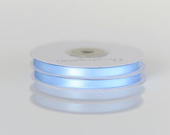 May include: Two spools of light blue satin ribbon on a white background. The ribbon is wrapped around the spools and the ends are visible. The spools are labeled "Decorative"