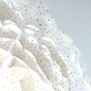 May include: White paper pom pom with gold glitter dots. The pom pom is made of multiple layers of tissue paper.