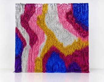 May include: A rectangular backdrop made of metallic fringe strips in vibrant colors including silver, hot pink, gold, royal blue, and deep purple. The strips are arranged in vertical, wavy, and abstract patterns, creating a textured surface.