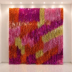 May include: A large, rectangular wall hanging composed of vertical strands of shimmering material. The colors include vibrant shades of orange, pink, magenta, and gold, creating a visually striking and festive display. The strands hang from top to bottom.