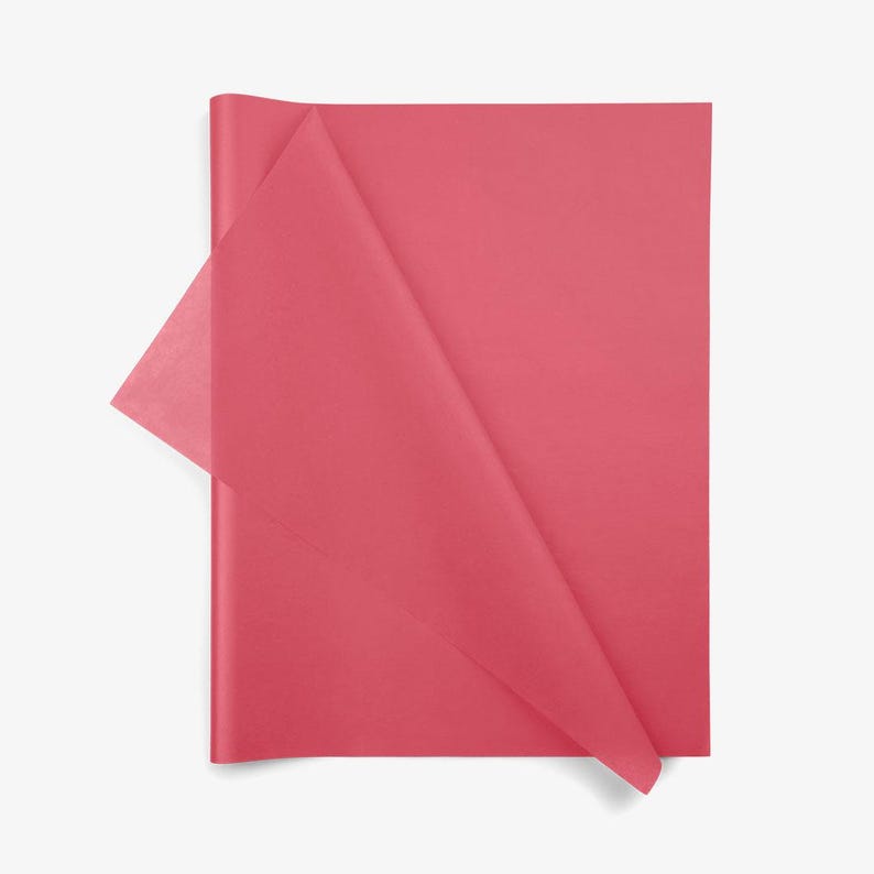 May include: A stack of rectangular sheets of thin, semi-translucent tissue paper in a solid, vibrant shade of pink. The top sheet is folded diagonally across the center, revealing the delicate, lightweight texture of the paper material.