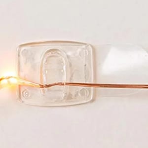 May include: A clear plastic hook with a copper wire attached to it. The hook is designed to be used with fairy lights or other decorative wires.