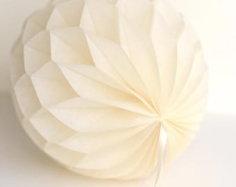 May include: A white paper honeycomb ball with a white ribbon attached. The ball is made of tissue paper and is folded into a honeycomb pattern. The ball is about 10 inches in diameter.