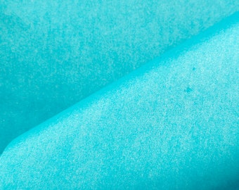 May include: A sheet of bright turquoise tissue paper with a delicate, semi-translucent texture. The paper is folded diagonally across the center, creating a soft, curved edge that highlights the vibrant, solid color and the thin, fibrous material.