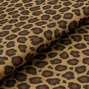 May include: Close-up of a fabric with a leopard print pattern. The fabric has a tan background with dark brown and black spots. The fabric is folded over, showing the texture and pattern.
