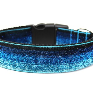 May include: A blue and black dog collar with a sparkly ombre design. The collar has a black plastic buckle.