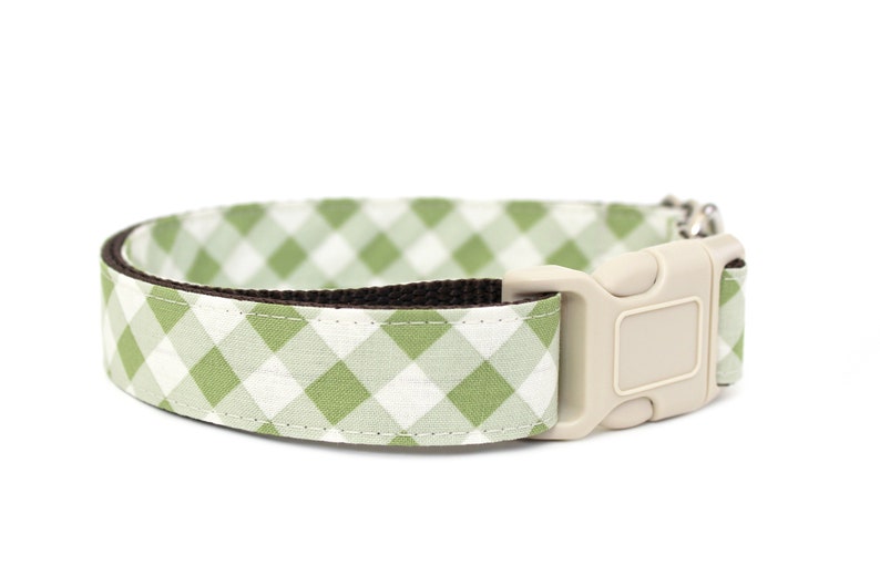 May include: A dog collar with a light green and white gingham pattern. The collar has a brown interior and a beige plastic buckle. The collar is designed for pets.