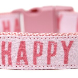 May include: Pink dog collar with the word "HAPPY" printed in pink on the front.